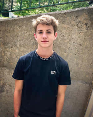 年輕男子穿黑色T恤，戶外靠著混凝土牆站立