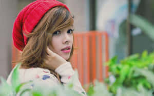 年輕女性戴紅色針織帽，在戶外與綠色植物一起若有所思地凝視。