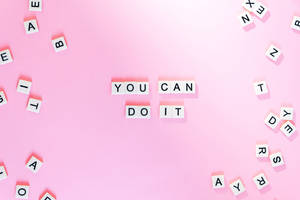 粉紅色背景上，白色字母瓷磚拼出「YOU CAN DO IT」，周圍散落著字母。