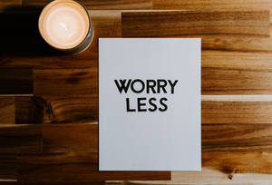 一支點燃的蠟燭旁邊放著一張寫有「WORRY LESS」的卡片，置於木質表面上。