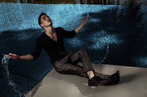 身穿黑衣的男子在泳池邊休息，用雙手潑水。