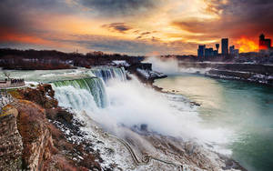 冬季日落時分的尼亞加拉大瀑布，霧氣升騰，城市天際線發出橙色光芒。