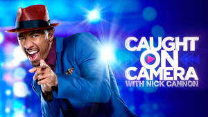 Nick Cannon 戴著紅色帽子和藍色西裝，背後有明亮燈光，指向觀眾。