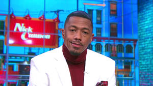 Nick Cannon 在脫口秀場景中身穿白色西裝外套和酒紅色高領毛衣。