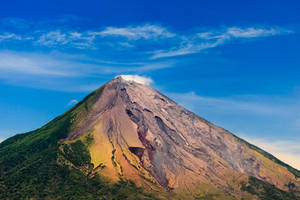 火山山脈，有綠色山坡和灰燼覆蓋的山脊，在藍天白雲下。