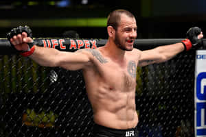 一位赤裸上身的MMA拳手在UFC八角籠內高舉雙臂慶祝勝利。
