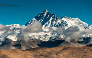 雪山峰頂高聳於雲層之上，前景是棕色丘陵