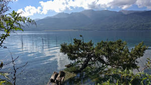 一個被山脈和樹木環繞的寧靜湖泊，天空部分多雲。 — 湖景 壁紙