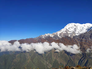 雪山峰在雲層之上聳立於藍天 — 山邊 壁紙