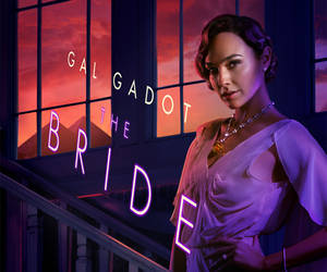 Gal Gadot 身穿紫色長裙，身後有霓虹新娘燈牌和日落山脈。