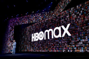 講者在HBO Max活動中進行演示，身後是一面電影海報牆。
