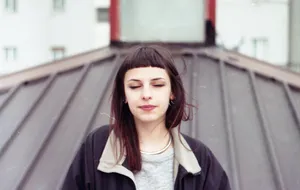 一位閉著眼睛的年輕女子站在城市環境中的金屬屋頂上。