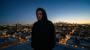 穿黑色連帽衫的男人在屋頂上俯瞰夜晚燈火通明的城市，星星可見。