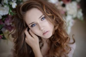 一位藍眼睛、捲髮的女子，被花朵環繞，輕輕地將下巴擱在手上。