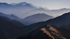 陽光突出山脊，層層霧氣籠罩的山峰逐漸消失在遠方。 — 5120x2880 壁紙