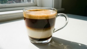 陽光照射的窗台上，一杯分層咖啡飲品放在玻璃杯中。