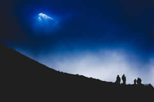 夜晚發光藍色山峰映襯下的登山者剪影。