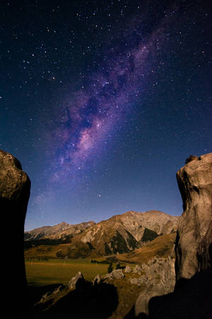銀河系在夜間山脈上方發光，由岩石框住