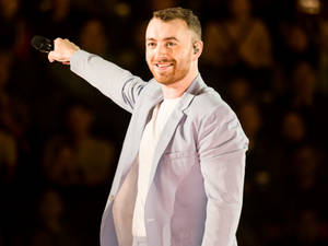 Sam Smith 在舞台上手持麥克風表演，並向觀眾微笑。