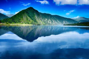 晴朗日子裡平靜的山間湖泊映照著藍天和綠丘。