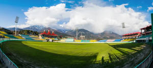 藍天下，板球場有綠色場地和山脈背景
