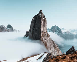一座鋸齒狀的山峰從雲層中浮現，下方是白雪覆蓋的山峰和寧靜的水面。