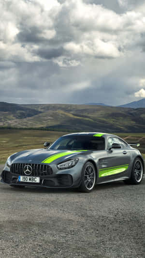 銀色 Mercedes-AMG GT 帶有綠色條紋，停在碎石地上，靠近丘陵，多雲天空。 — 山脈 壁紙