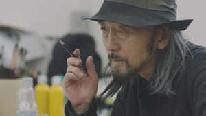 一位年長藝術家，灰色頭髮，戴著帽子，在畫室裡拿著鉛筆。