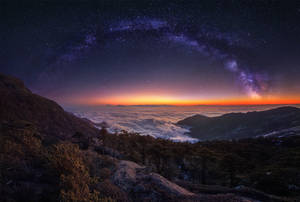 山峰在星空下升起於雲海之上，伴隨著銀河
