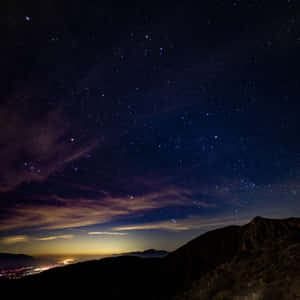 山上的星空夜晚，下方有遠處的城市燈光。 — iPad 第10代 壁紙
