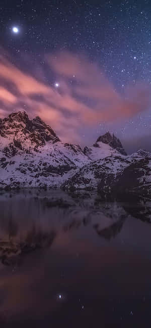 積雪的山峰在繁星點點的夜空下倒映於平靜的水面，伴隨著粉紅色的雲朵。
