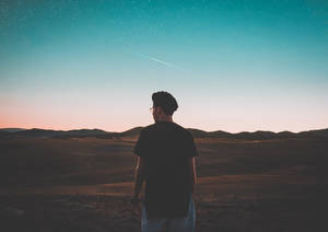 一個剪影中的男人站在沙漠中，觀看暮色天空中的流星。