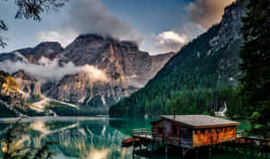 湖邊碼頭上的木屋，有山景倒影和森林背景 — 湖景 壁紙