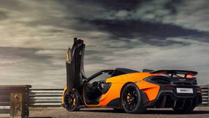 橙色McLaren 600LT跑車，車門打開，停在多雲天空下的賽道上。