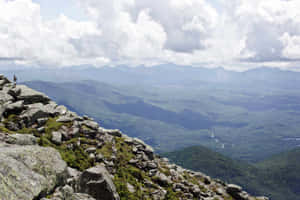 一個人站在岩石山峰上，俯瞰著森林覆蓋的山谷。 — 雲 壁紙