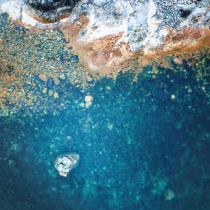 從高空俯瞰，碧綠的海水與岩石海岸交匯，散落著鵝卵石和一個小島。