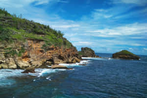 海岸懸崖，海浪拍打，綠色植被，部分多雲的天空。 — MacBook Pro M2 壁紙