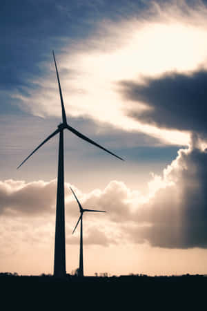 兩座風力渦輪機在日落天空和戲劇性雲層的襯托下形成剪影。