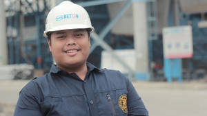 一位戴著安全帽、身穿藍色制服的建築工人在混凝土廠對著鏡頭微笑。