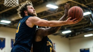 兩名男性籃球運動員在體育館籃框下爭球。