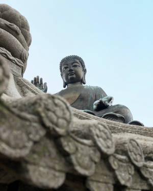 一座大型青銅佛像坐在石造建築上，天空蒼白。