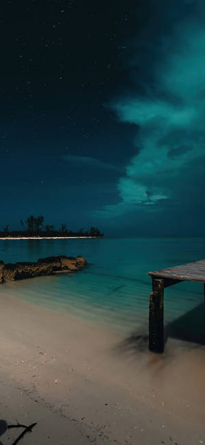 寧靜海灘上的木製碼頭夜景，星空下伴有發光的青綠色雲彩。