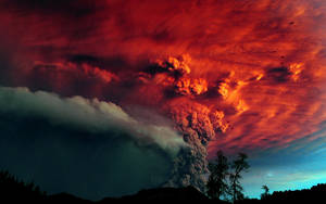 火山爆發，熾熱的火山灰雲映襯著暮色天空和樹木剪影。