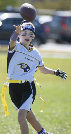 穿著 Ravens 美式足球裝備的小女孩在草地上拋出一個美式足球。 — NFL 美式足球 GIF 壁紙