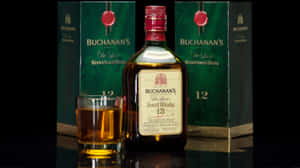 Buchanan's 威士忌酒瓶和酒杯置於深色反光表面，旁邊有綠色盒子。