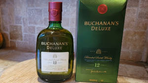 Buchanan's Deluxe 威士忌瓶和盒子放在木桌上，背景是石牆