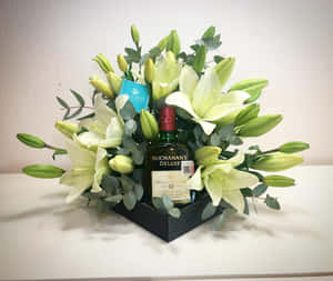 威士忌瓶被白百合和綠色植物環繞，放在黑色禮盒中。