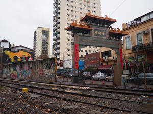 城市環境中的中式牌坊，帶有塗鴉和火車軌道，天空灰暗