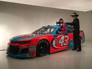 NASCAR車手在賽車中與身穿黑色西裝和帽子的男士在攝影棚擺姿勢。