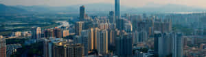 日落時分現代城市的全景視圖，背景是山脈。 — 32:9 壁紙